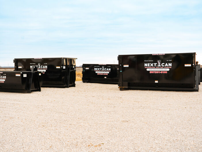 Multiple black Next Can dumpsters on gravel lot under blue sky.
