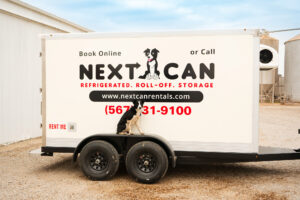 Side view of a white Next Can refrigerated trailer featuring the company logo and a dog mascot, parked in a rural setting.