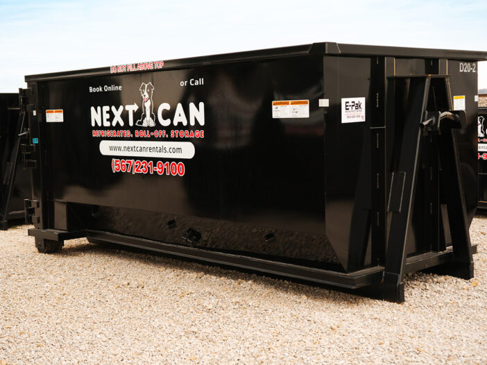 Side view of a large black Next Can 20 yard dumpster on a gravel lot, prominently displaying the company's contact information and logo featuring a dog silhouette.