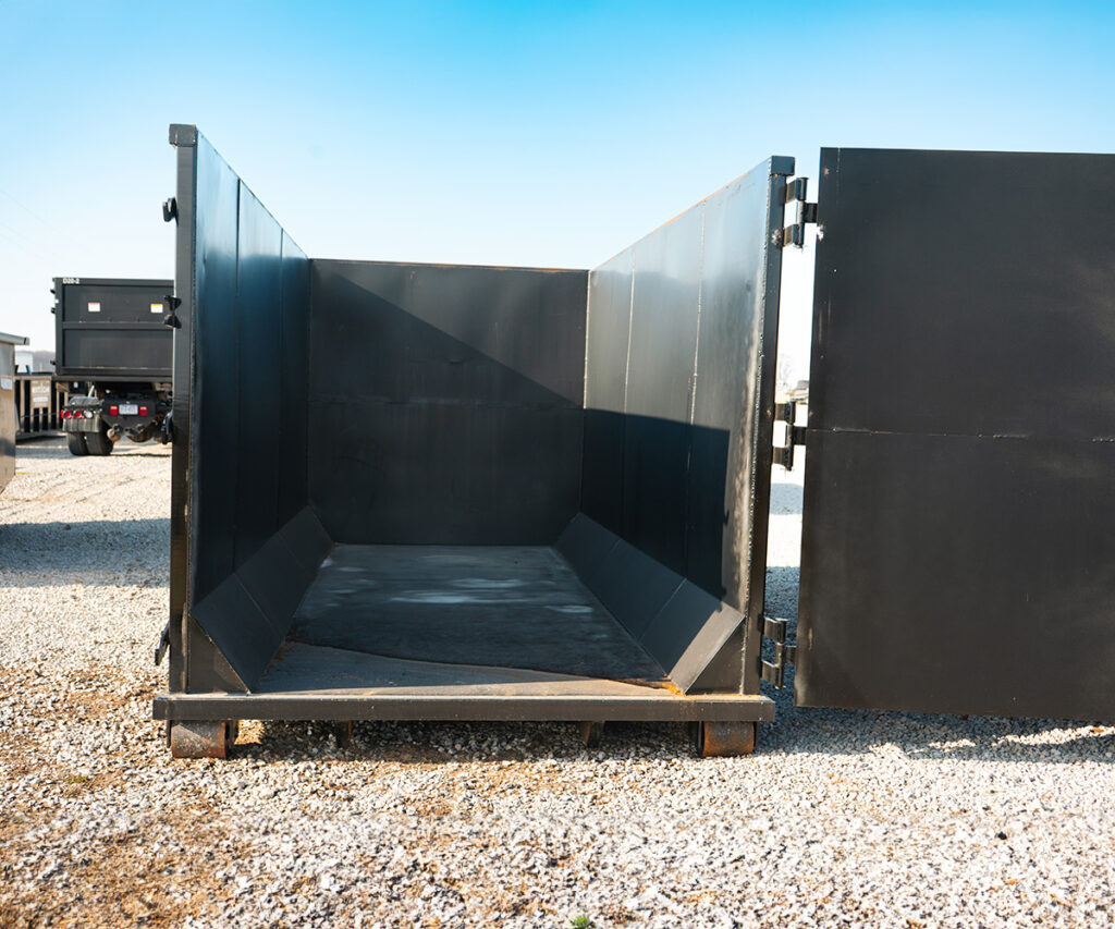 Close-up view of an open, empty black roll-off dumpster from Next Can, positioned on a gravel lot.