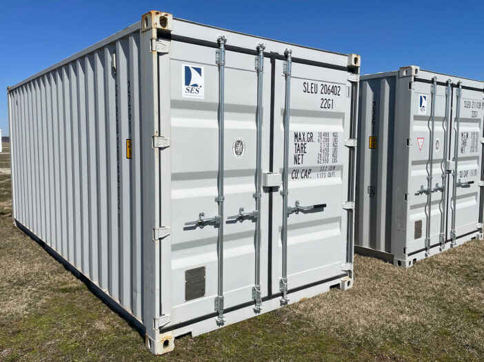 Two white storage containers on grass under clear blue sky.