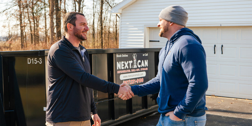 Two men shaking hands in front of a Next Can Rentals dumpster.