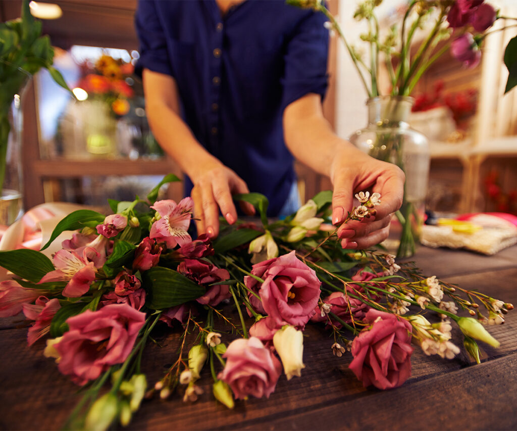 Florist arranging fresh flowers on a wooden table indoors.