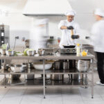 Chefs preparing food in a commercial kitchen with stainless steel equipment.