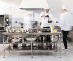 Chefs preparing food in a commercial kitchen with stainless steel equipment.