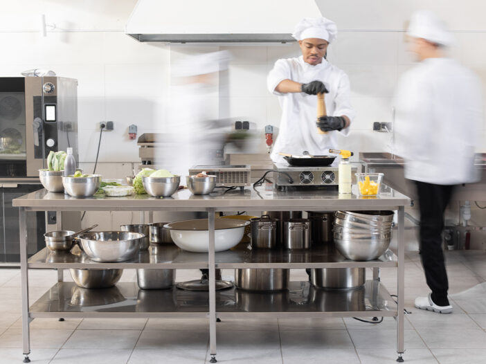 Chefs preparing food in a commercial kitchen with stainless steel equipment.