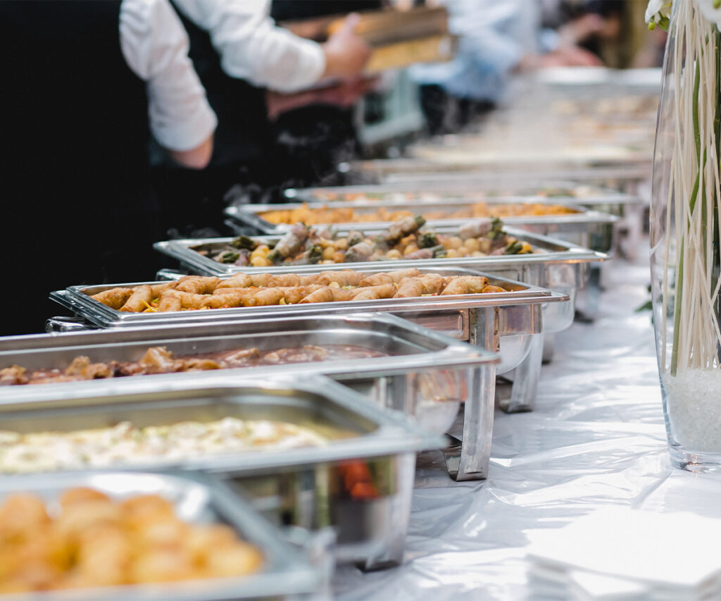 Buffet table with catering trays of hot food at an event.