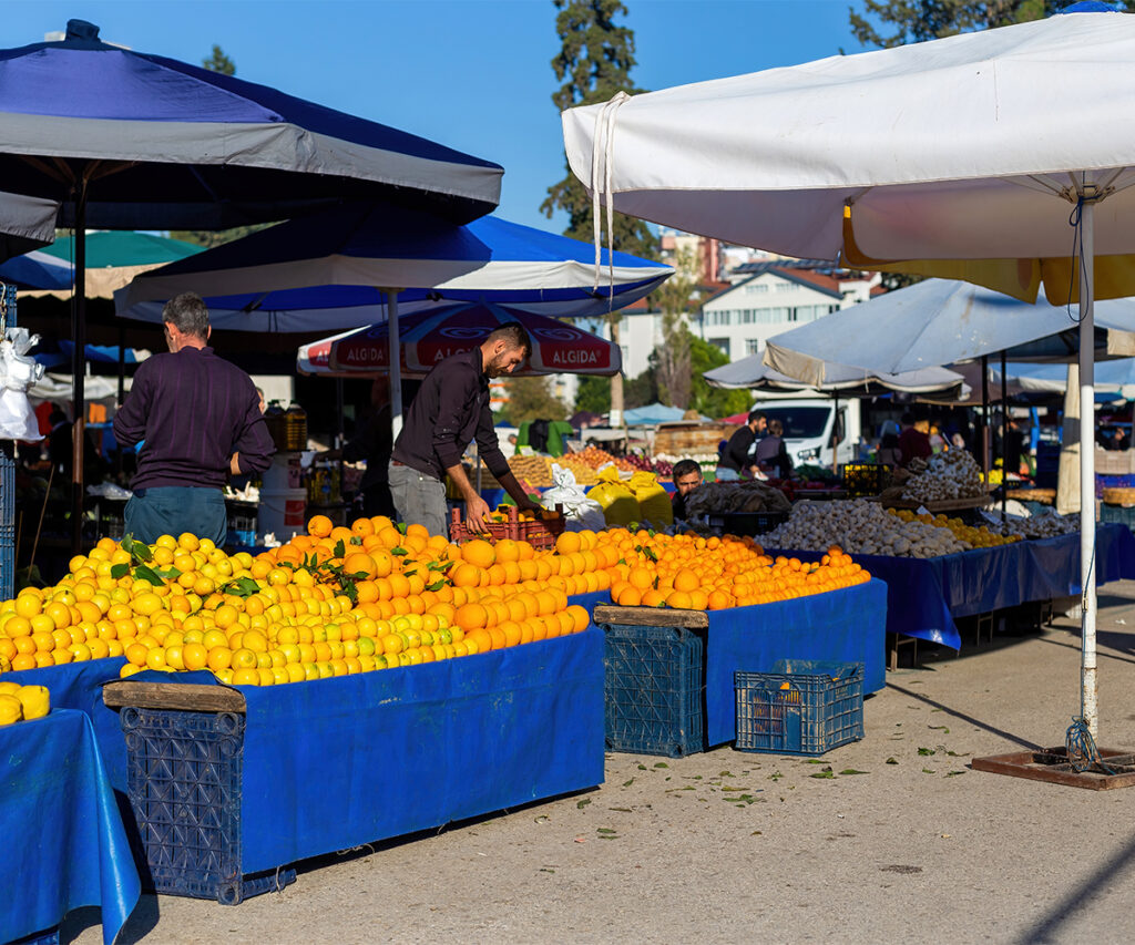 Vendors selling fresh oranges and produce at an outdoor farmer’s market.